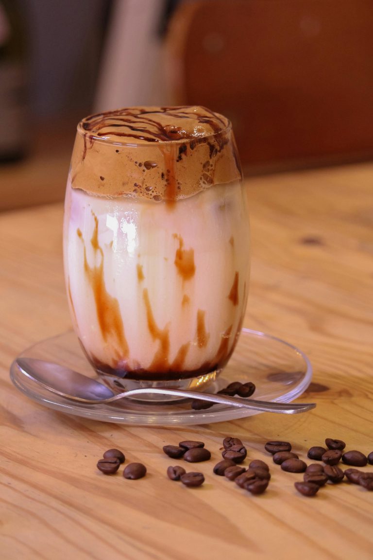 A caramel iced coffee with cream and caramel drizzle in a glass on a wooden table.